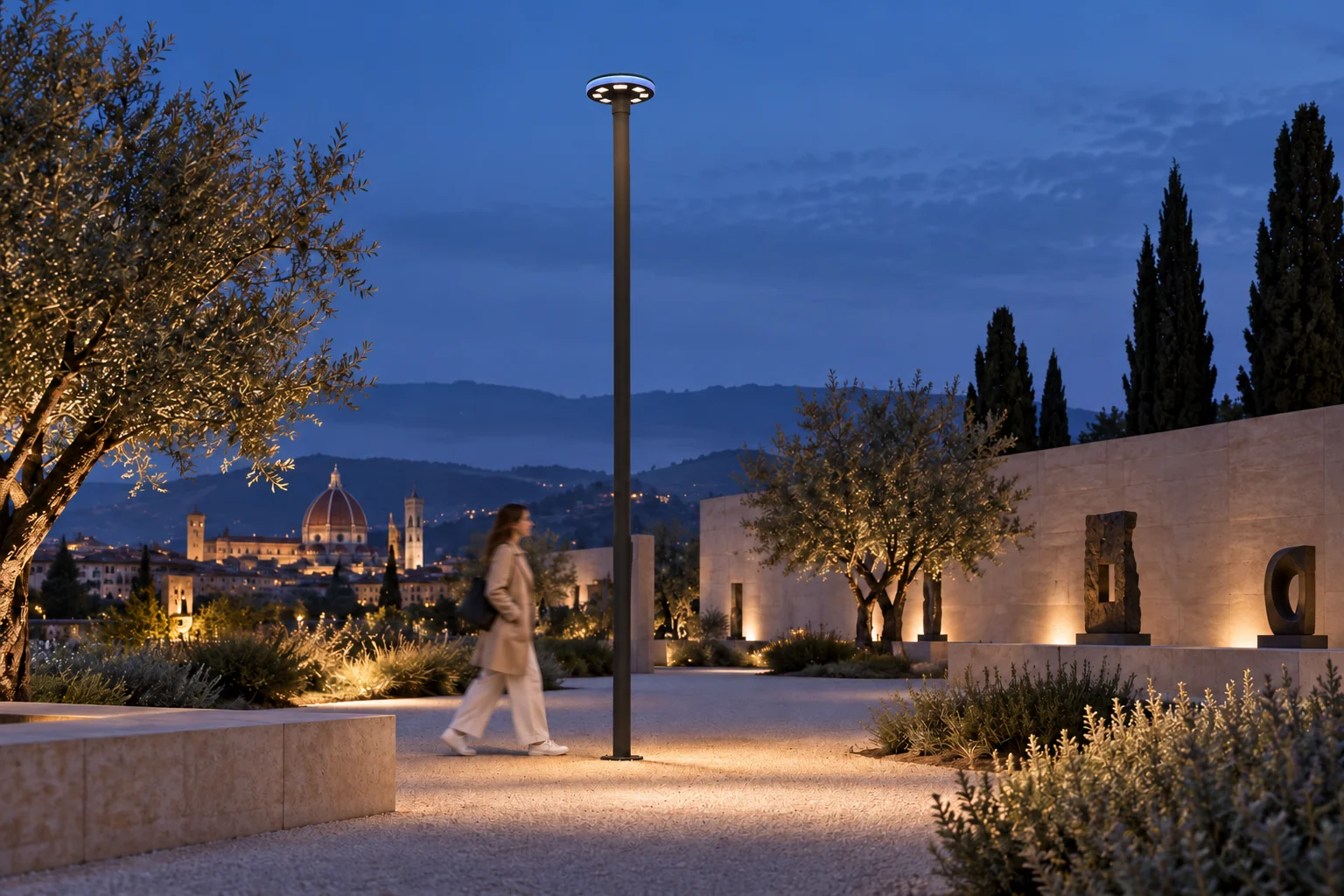 Evening cultural park concept with a pole-mounted P.A.D. URBAN luminaire along a path and a person walking