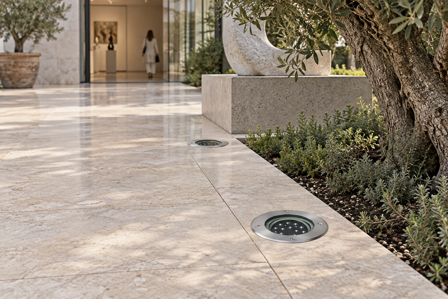 Switched-off fixtures flush with the paving, with a four-screw metal rim and optical group. Diameter and mounting are illustrative; the photograph identifies no series code.